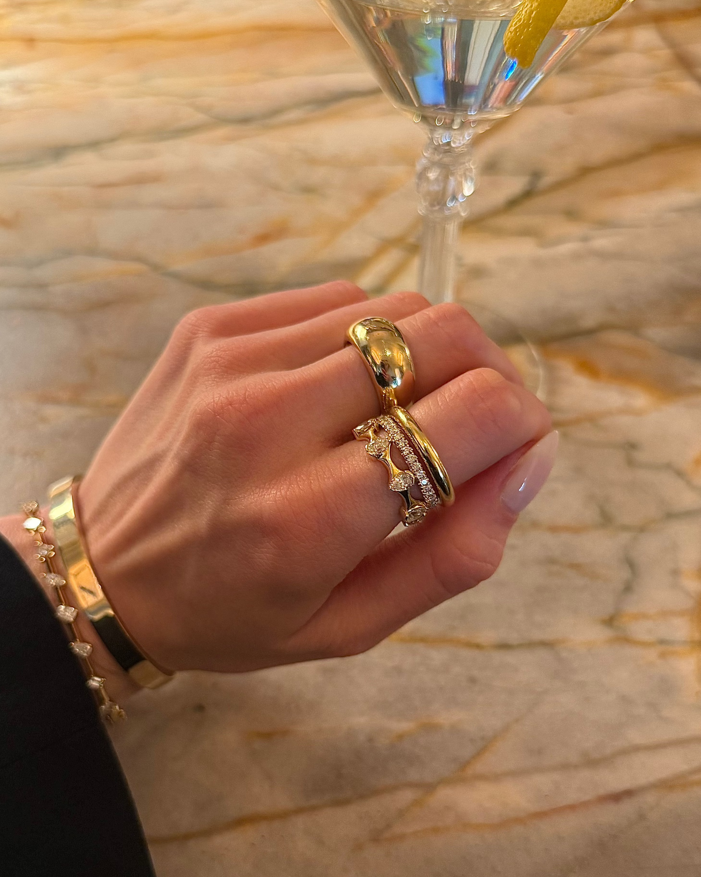 Lifestyle photo of woman wearing J.Tyler Jewelry Crown Eternity Band in 18K gold with pear-shaped diamonds, stacked with matching rings while next to elegant martini glass.