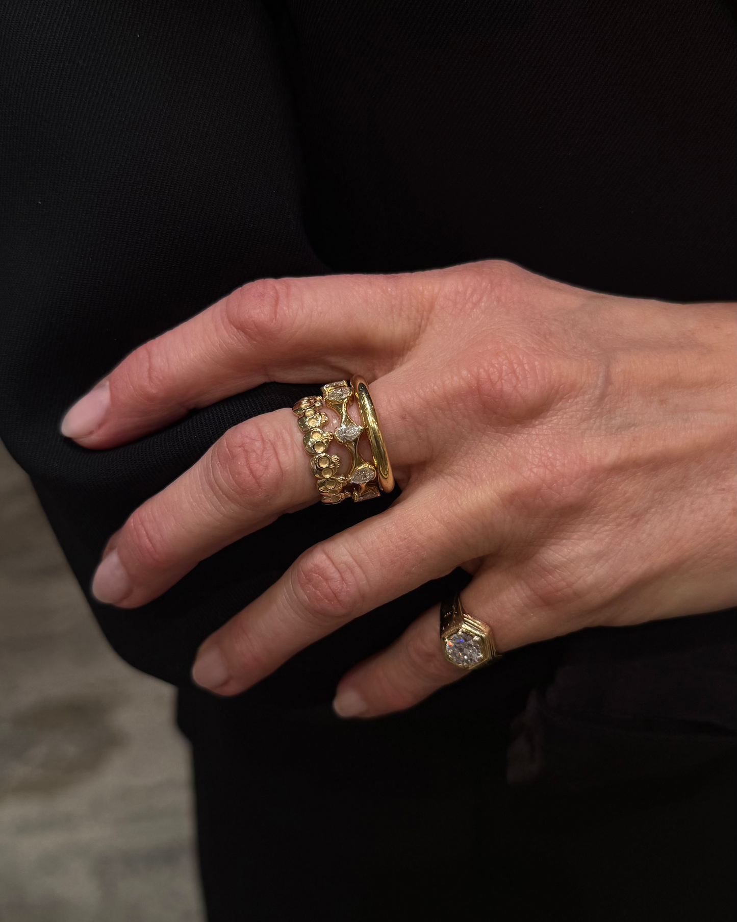 Close-up of woman's hands wearing J.Tyler Jewelry Crown Ring in 18K yellow gold with pear-shaped diamonds, showcasing the twisted band design and sculptural silhouette against black clothing