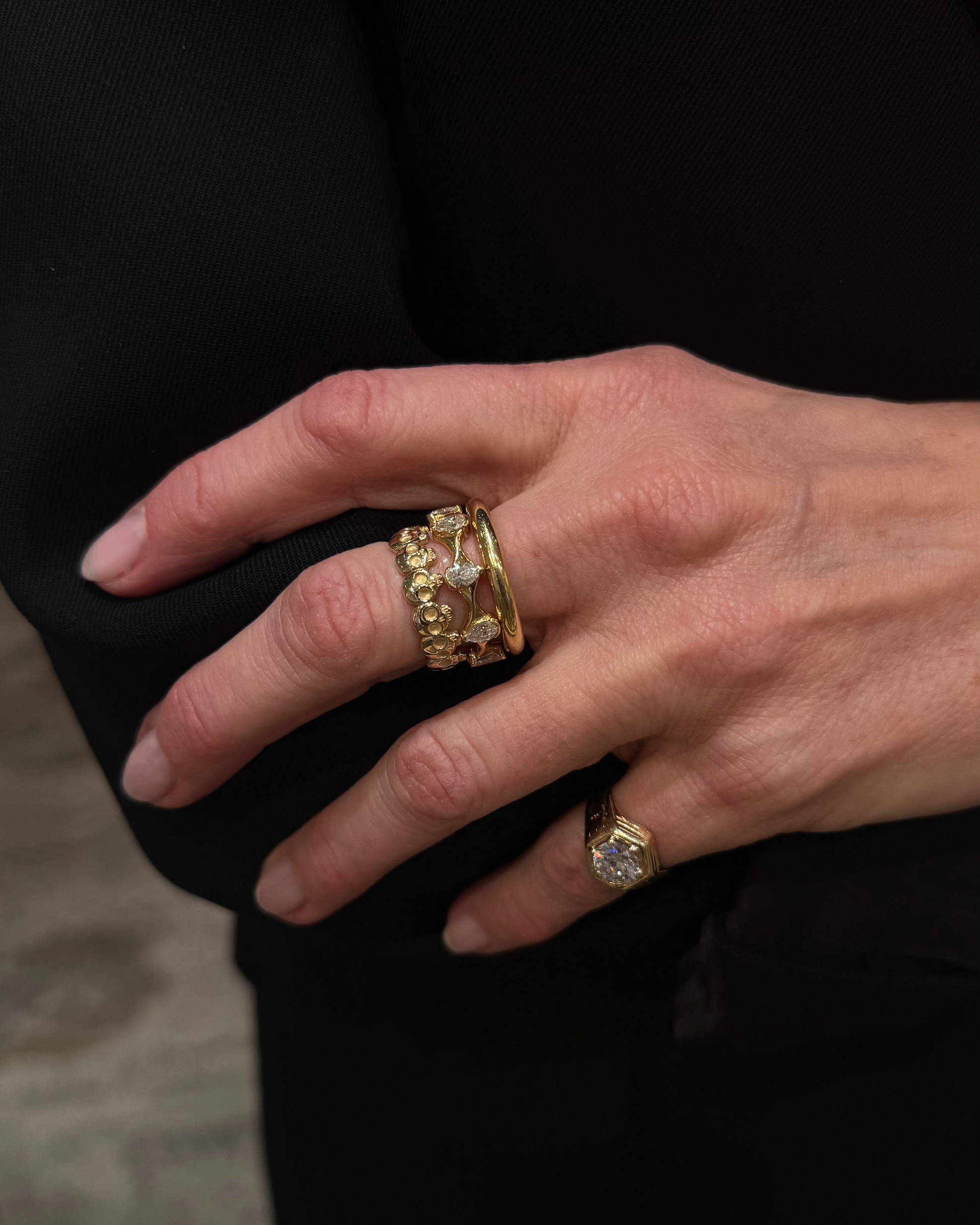 Close-up of woman's hands wearing J.Tyler Jewelry Crown Ring in 18K yellow gold with pear-shaped diamonds, showcasing the twisted band design and sculptural silhouette against black clothing